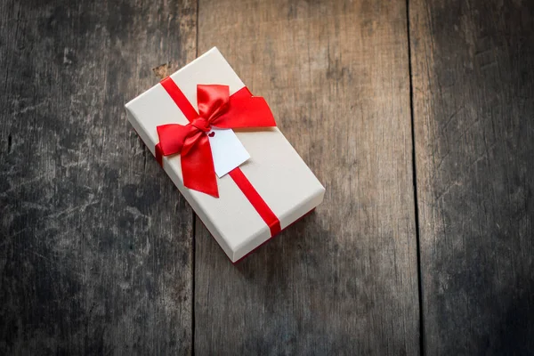 Ahşap arka plan üzerinde kırmızı yay ile bağlı krem renkli hediye kutusu