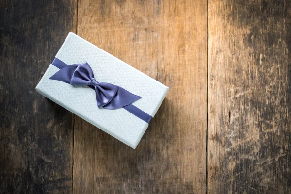 Boîte cadeau de couleur blanche attachée avec arc bleu sur fond en bois — Photo
