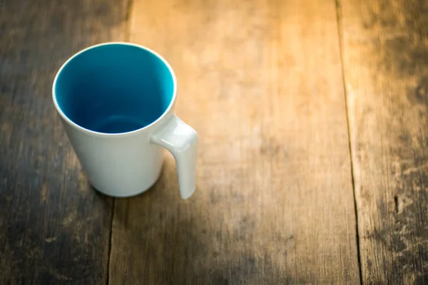 Weiße Tasse innen blau auf hölzernem Hintergrund — Stockfoto