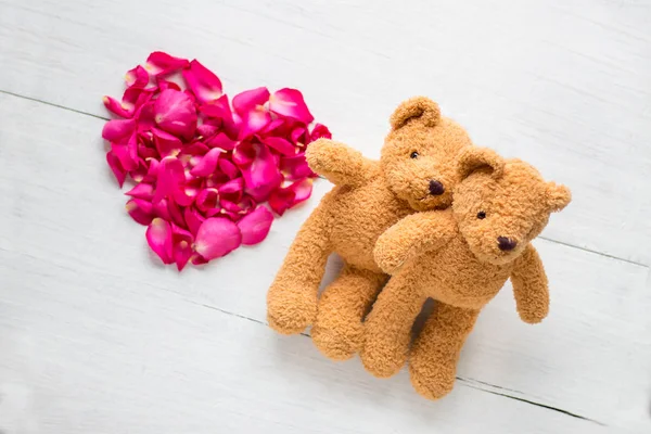 Teddy bear couple and pink petals heart shape on white wooden background. Valentine background. — Stock Photo, Image