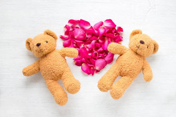 Teddybär-Paar und rosa Blütenblätter Herzform auf weißem Holzhintergrund. Valentin-Hintergrund. — Stockfoto