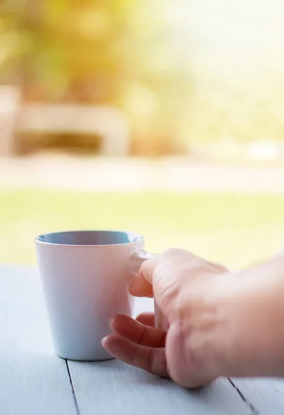 Hand hebt morgens eine weiße Tasse Kaffee über dem grünen Garten auf. — Stockfoto
