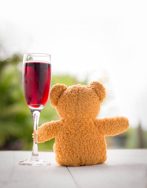 valentine concept. teddy bear with red wine glass over bokeh green garden background.