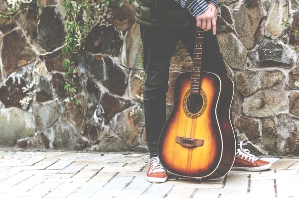 Jeune homme avec une guitare près du mur de pierre — Photo