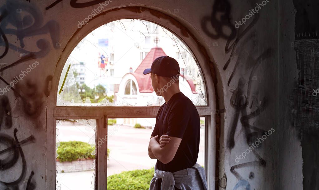 young man looks into an old broken window