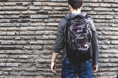  genç bir duvarının yakınında bekleyen bir sırt çantası ile