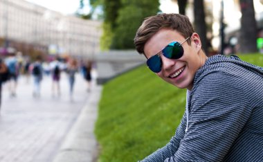 Çimenlerin üzerinde oturan gözlüklü yakışıklı genç adam