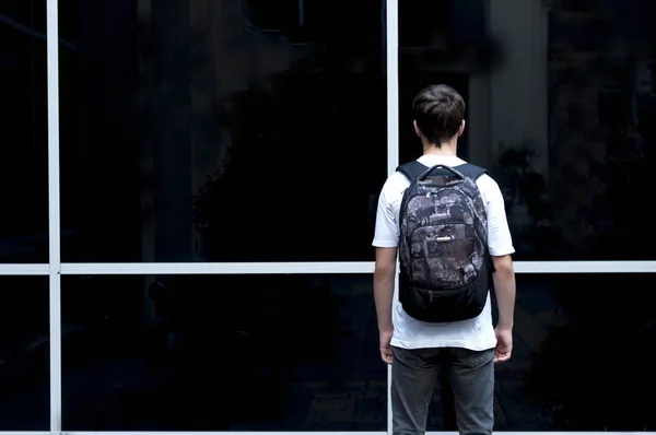 Jovem com uma mochila olhando para uma janela de vidro — Fotografia de Stock