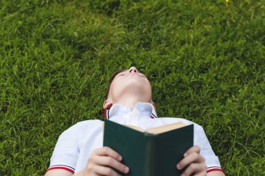 Çim üzerinde yalan elinde bir kitapla genç
