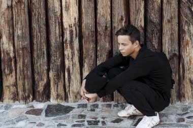 Ahşap bir duvara yakın oturan yakışıklı genç adam