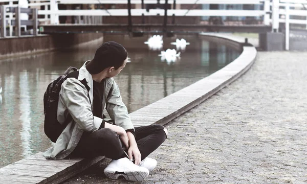 göl yakınındaki kaldırımda oturan genç adam