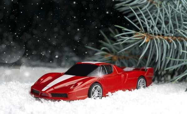 small, red, toy car in the snow near the fir-tree