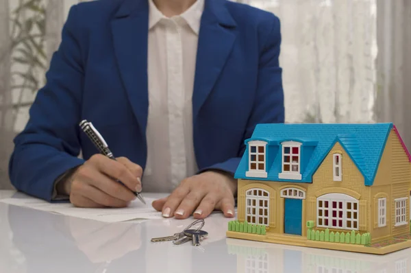 Frau mit Hausmodell und Stift unterschreibt Vertragsdokument — Stockfoto