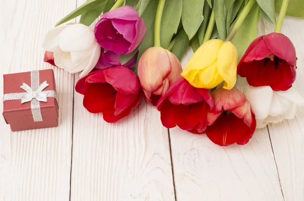 Ramo de tulipanes con un regalo sobre tabla de madera rústica — Foto de Stock