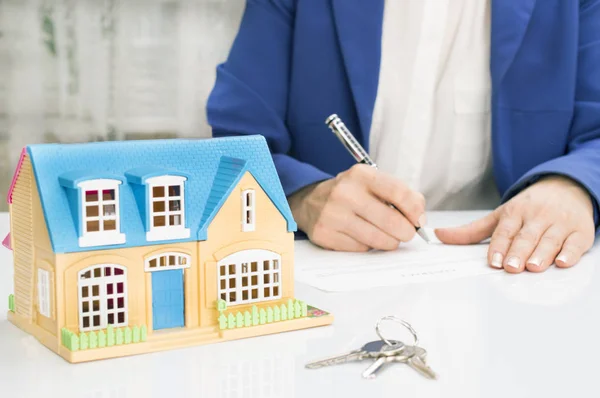 Mujer con modelo de casa y documento de contrato de firma de pluma —  Fotos de Stock