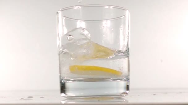 Σταγόνες λεμονιού σε ένα ποτήρι με νερό αργή κίνηση — Αρχείο Βίντεο