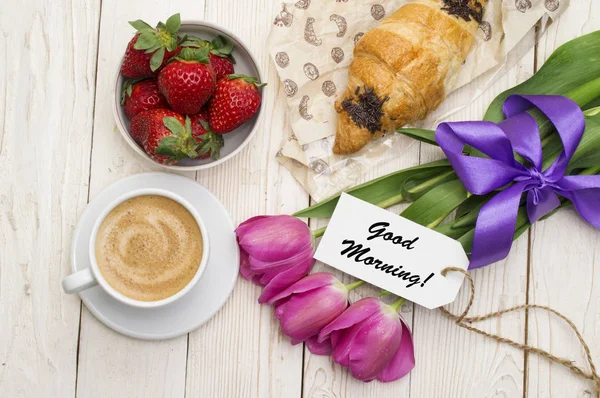 Cup of coffee, tulips, croissant, strawberries and Good morning massage on wooden background