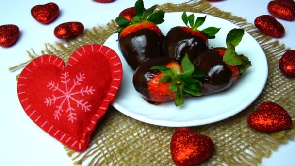 Un plato de fresas cubiertas de chocolate afuera en una mesa con corazones rojos, día de San Valentín . — Vídeos de Stock