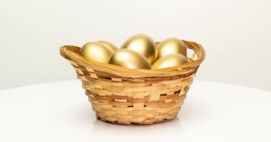 Beyaz arka planda sepetteki altın yumurtalar. Altın yumurtalar yakın plan, Paskalya, bahar, yatırım ve emeklilik konsepti. Kamera döndürmesi