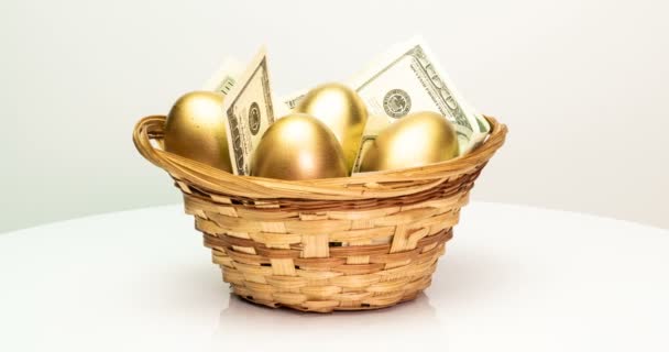 Χρυσά αυγά και δολάρια σε ένα καλάθι σε λευκό φόντο. Χρυσά αυγά σε πρώτο πλάνο, Πάσχα, άνοιξη, επενδύσεις και συνταξιοδότηση έννοια. Περιστροφή κάμερας — Αρχείο Βίντεο