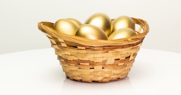 Золотые яйца в корзине на белом фоне. Золотые яйца крупным планом, съедобные, весенние, инвестиционные и пенсионные концепции. Вращение камеры — стоковое видео