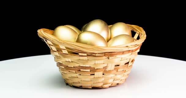 Золотые яйца в корзине на черном фоне. Золотые яйца крупным планом, съедобные, весенние, инвестиционные и пенсионные концепции. Вращение камеры — стоковое видео
