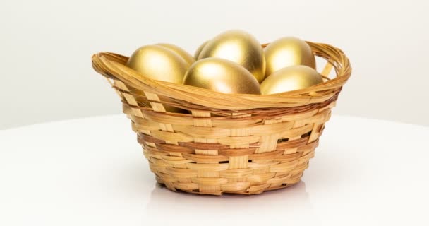 Zlatá vejce v košíku na bílém pozadí. Zlatá vejce detailní, velikonoční, jarní, investiční a důchodové koncepce. Rotace fotoaparátu — Stock video