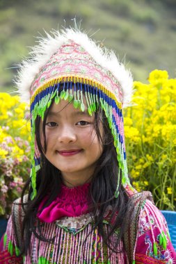 Ha Giang, Vietnam - 14 Aralık 2019: Geleneksel elbiseli Hmong azınlık kız Tham Ma dağ geçidinin arkasında duran renkli çiçekler, Dong Van bölgesi.