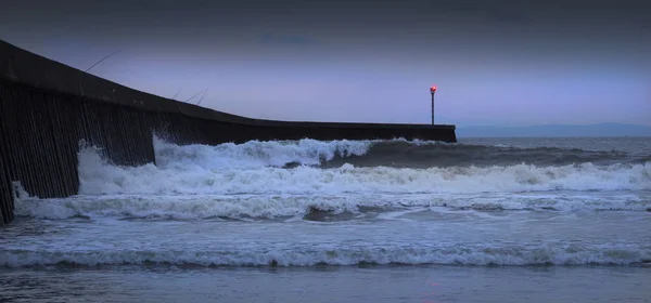 High tide fishing rods and breaking waves at blue hour on the West Pier on Swansea Bay, South Wales, UK