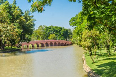 Yazın büyük kentin merkezindeki parkın manzarası. Baharda parktaki köprü güneşli bir günde ortada bir göl ve tropikal bölgede yeşil ağaçlar