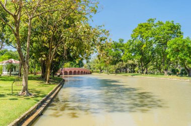 Yazın büyük kentin merkezindeki parkın manzarası. Baharda parktaki köprü güneşli bir günde ortada bir göl ve tropikal bölgede yeşil ağaçlar