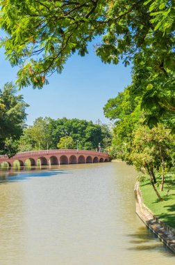 Yazın büyük kentin merkezindeki parkın manzarası. Baharda parktaki köprü güneşli bir günde ortada bir göl ve tropikal bölgede yeşil ağaçlar
