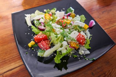 Restorandaki ahşap bir masada siyah kare bir tabakta Yunan salatası.