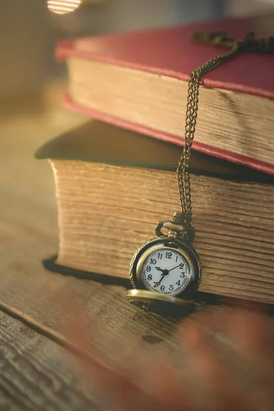 yakın çekim eski cep saati ile sabah ışığında kitap yığını