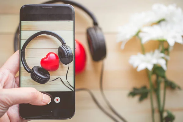 Smartphone cep telefonu ile fotoğraf kalp için tuşuna basarak parmak ahşap arka plan ve kopya alanı kavramı, aşk ve müzik için müzik dinle