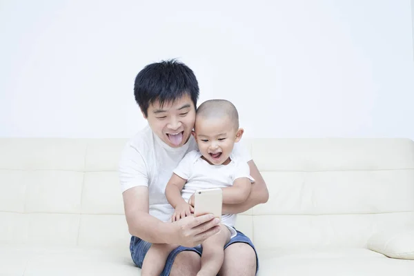 Chinesischer Vater und Sohn machen Selfie auf Sofa — Stockfoto