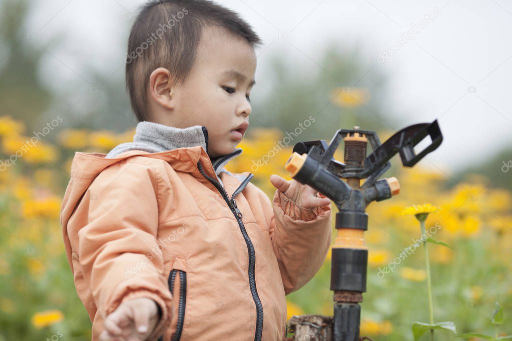 Cute baby boy playing a faucet in blossoms