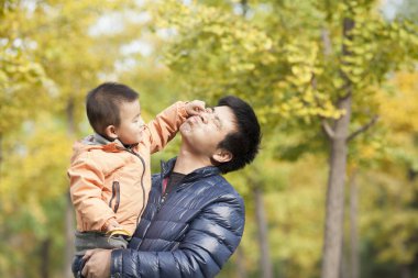 Mutlu gerçek baba ve oğul ginkgo ağaçları önünde oynarken