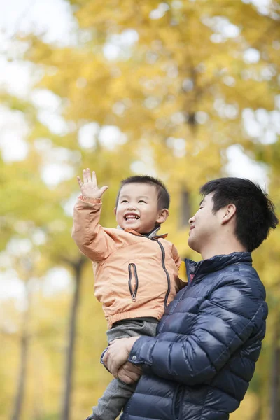 Feliz verdadero padre e hijo jugando frente a los árboles de ginkgo —  Fotos de Stock