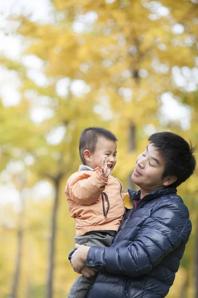 Mutlu gerçek baba ve oğul ginkgo ağaçları önünde oynarken