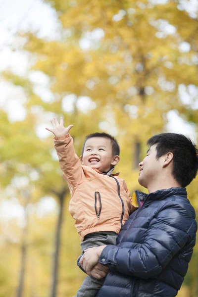 Feliz verdadero padre e hijo jugando frente a los árboles de ginkgo —  Fotos de Stock