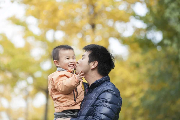 Mutlu gerçek baba ve oğul ginkgo ağaçları önünde öpüşme