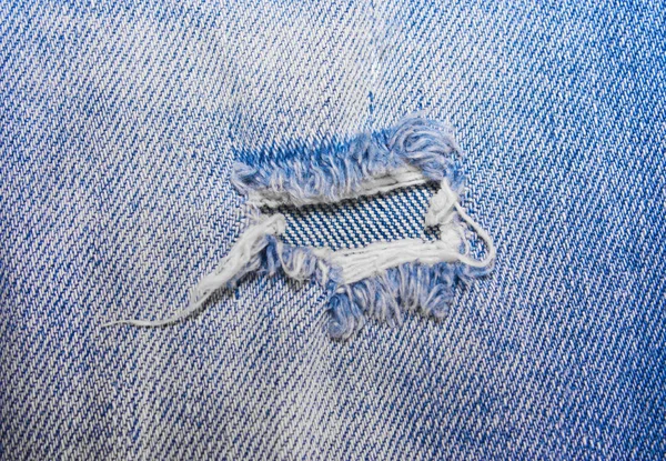 Дыра на синих джинсах — стоковое фото