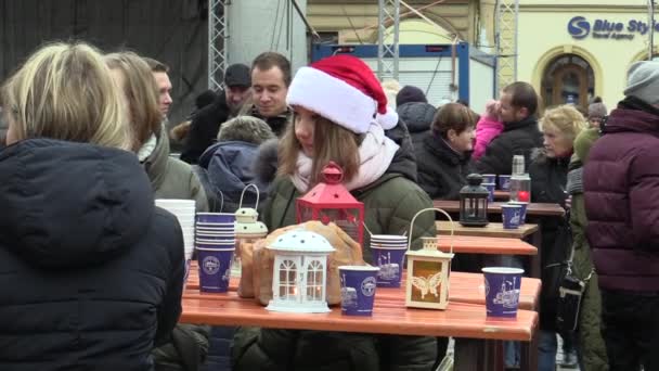 ตลาดคริสต์มาส บูธขายเครื่องดื่มแอลกอฮอล์พร้อมน้ําผลไม้ ผู้คนซื้อเครื่องดื่มในถ้วย และในความใจกว้าง ผู้หญิงที่มีหมวกซานตาคลอส แสงเบธเลเฮม — วีดีโอสต็อก