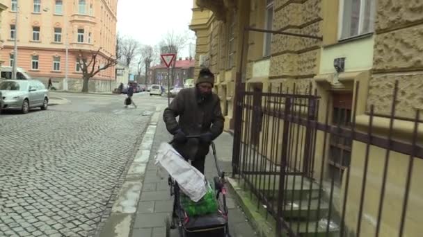 Olomouc, Česká republika, 5. března 2018: Autentické chudý bezdomovec chodí steadycam ulicí s vozík kočár, ve kterém má plastová láhev vína. Velmi reálná, život na ulici — Stock video