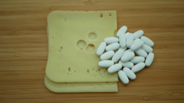 Calcium tablets pills medical capsules white pile and Emmentaler hard cheese containing calcium supplement Swiss matured with milk bacterium, vitamin D, wooden board background