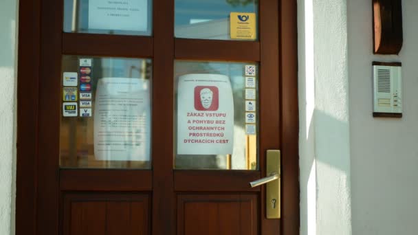 OLOMOUC, REPÚBLICA CHECA, 20 DE ABRIL DE 2020: Entrada Czech Post branch door, banner respecting governments ban movement without respiratory safety scarf shawl protective restricted people — Vídeos de Stock