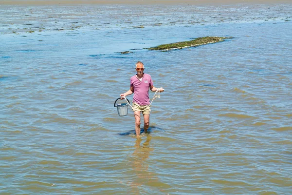 Ο άνθρωπος περπατώντας στα ρηχά νερά με κουβά με μύδια συλλέγονται fr — Φωτογραφία Αρχείου