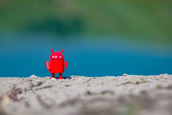 Kırmızı küçük oyuncak android göl kıyısında duruyor