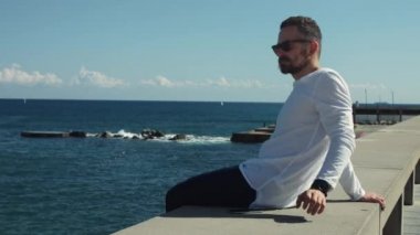 Güneşli bir günde denizin önünde oturan adam